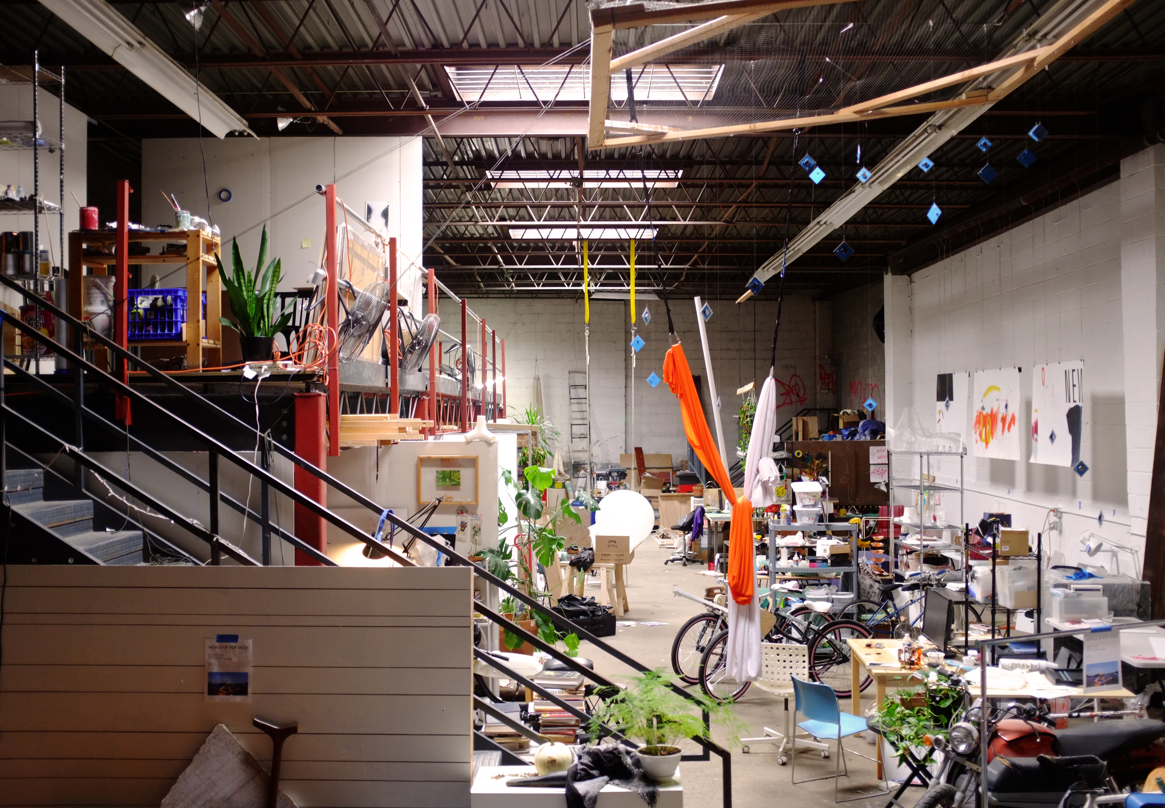 Soft Surplus in the morning, days after the New York Tech Zine Fair. Image description: The Soft Surplus studio space which is a warehouse full of desks, boxes, storage units and green plants among other things.