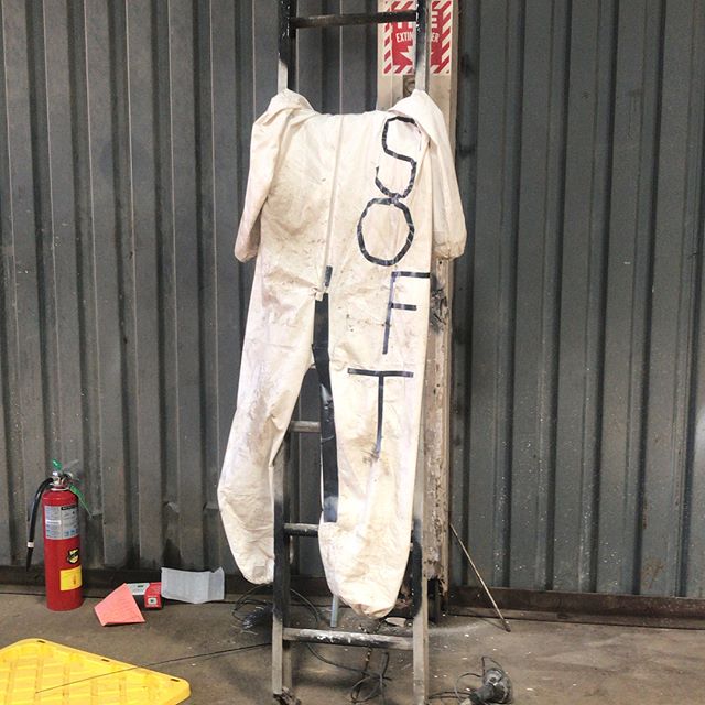 Image description: A photo of a dirty white jumpsuit with the word “soft” written in capital sans serif letters.